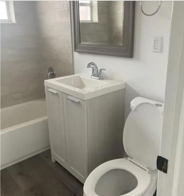 full bathroom with tiled shower / bath, vanity, toilet, and hardwood / wood-style floors