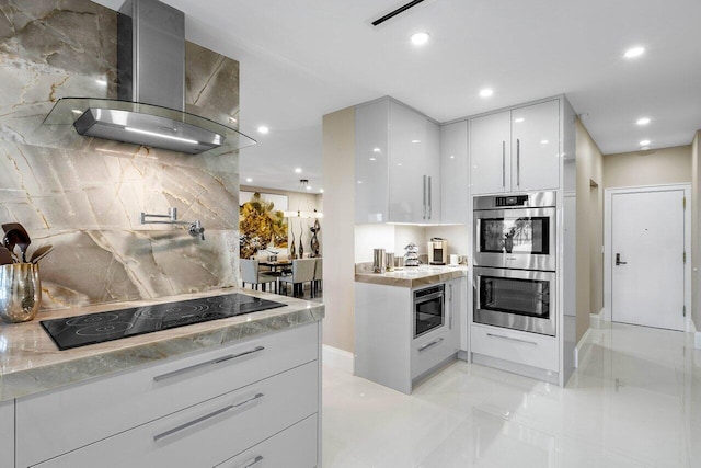 kitchen featuring black electric stovetop, stainless steel double oven, light stone counters, wall chimney exhaust hood, and tasteful backsplash