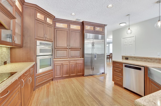 kitchen featuring decorative light fixtures, appliances with stainless steel finishes, light wood-type flooring, and light stone counters