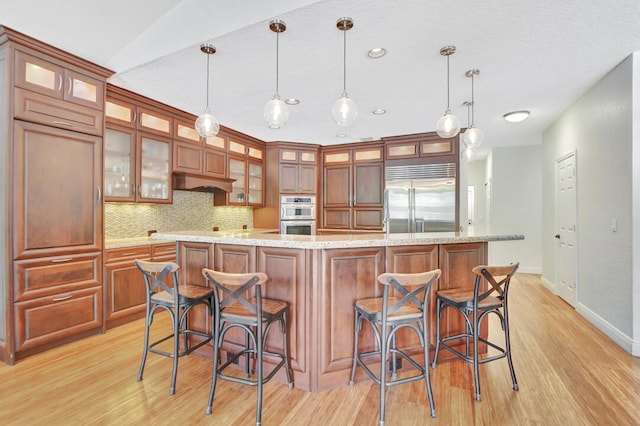 kitchen featuring light hardwood / wood-style flooring, backsplash, hanging light fixtures, appliances with stainless steel finishes, and a breakfast bar