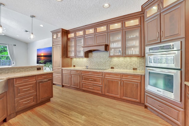 kitchen with stainless steel double oven, hanging light fixtures, light hardwood / wood-style floors, and vaulted ceiling