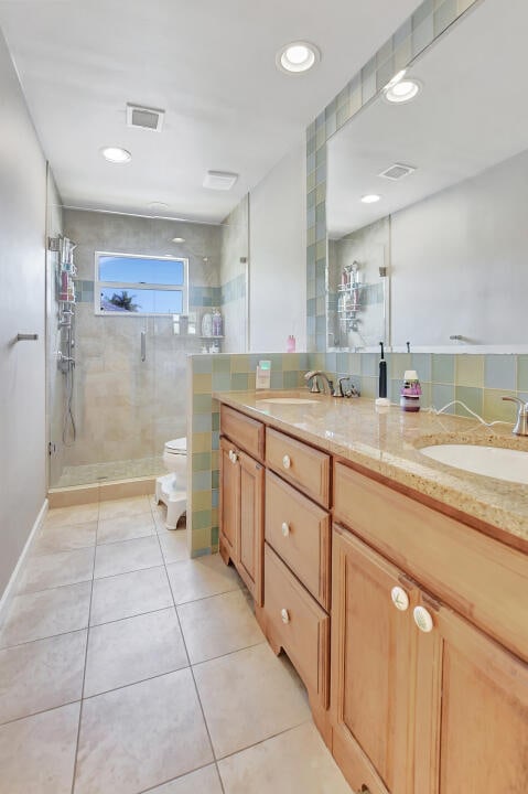 bathroom with tile walls, dual bowl vanity, toilet, tile floors, and a tile shower