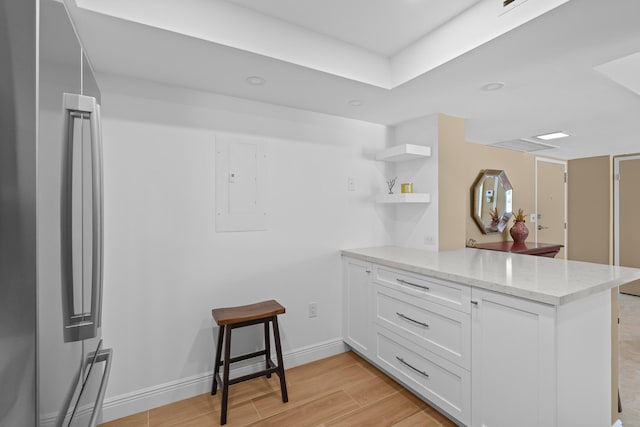 kitchen featuring white cabinetry, kitchen peninsula, light wood-type flooring, and light stone counters