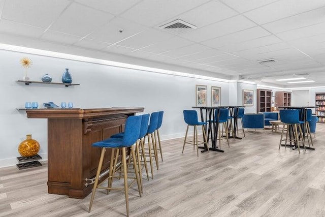 bar featuring light wood-type flooring and a drop ceiling