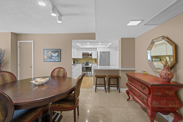 dining area featuring a textured ceiling, light tile floors, and rail lighting