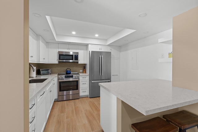 kitchen with light wood-type flooring, appliances with stainless steel finishes, white cabinets, backsplash, and a raised ceiling