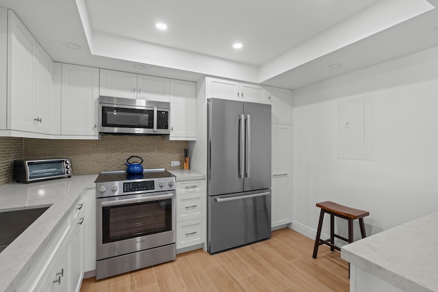 kitchen with appliances with stainless steel finishes, white cabinets, tasteful backsplash, and light hardwood / wood-style flooring