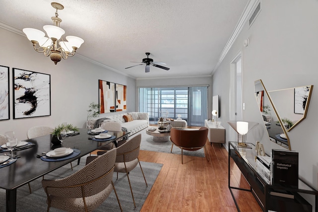 dining space featuring a textured ceiling, ceiling fan with notable chandelier, wood-type flooring, and crown molding