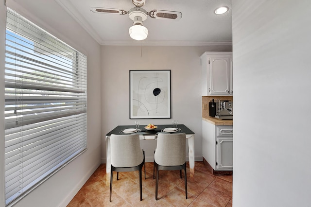 tiled dining area with ceiling fan and crown molding