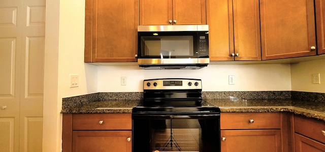 kitchen with dark stone counters, kitchen peninsula, appliances with stainless steel finishes, sink, and light tile floors