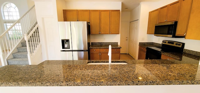 kitchen with kitchen peninsula, stainless steel appliances, dark stone countertops, light tile floors, and sink