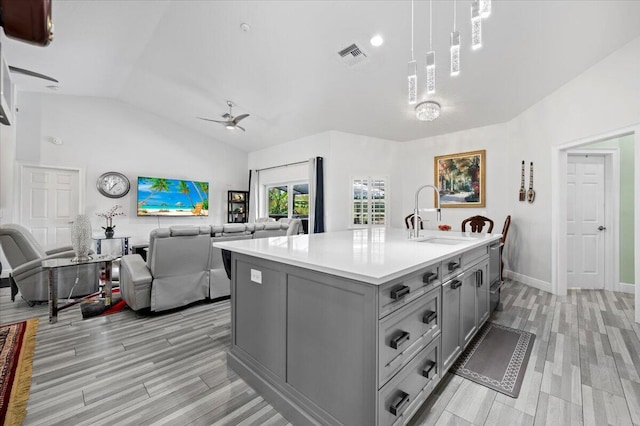 kitchen with vaulted ceiling, sink, light hardwood / wood-style flooring, and a kitchen island with sink