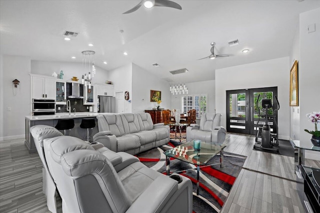 living room featuring light hardwood / wood-style flooring, ceiling fan with notable chandelier, high vaulted ceiling, sink, and french doors