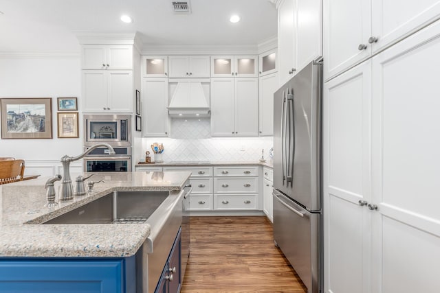 kitchen with custom range hood, stainless steel appliances, white cabinetry, and crown molding