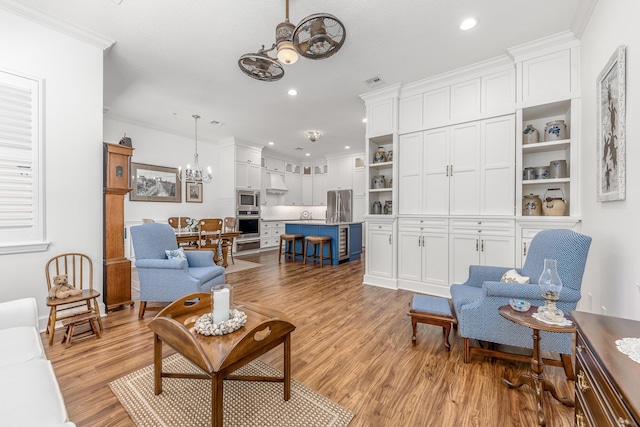 living room with ceiling fan with notable chandelier, light wood-type flooring, and crown molding