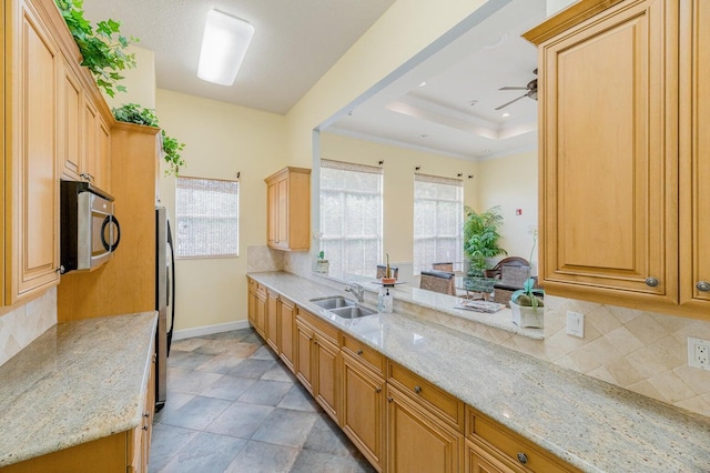 kitchen featuring light stone countertops, sink, ceiling fan, stainless steel appliances, and a raised ceiling