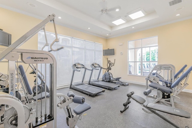 exercise room featuring ceiling fan, a raised ceiling, and ornamental molding