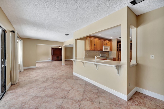 kitchen featuring a textured ceiling, kitchen peninsula, a kitchen breakfast bar, stainless steel electric range oven, and decorative backsplash