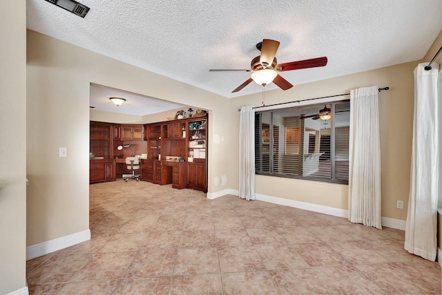 unfurnished living room with built in desk, a textured ceiling, and ceiling fan