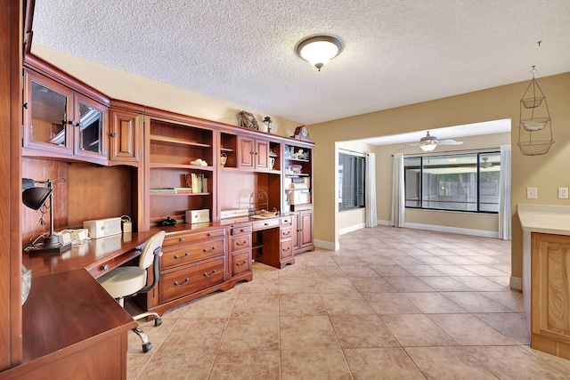 tiled home office featuring a textured ceiling, built in desk, and ceiling fan