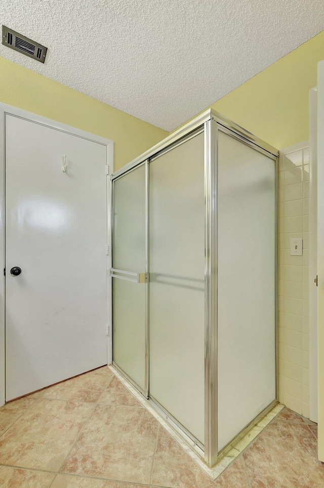 bathroom featuring a shower with door, tile patterned floors, and a textured ceiling