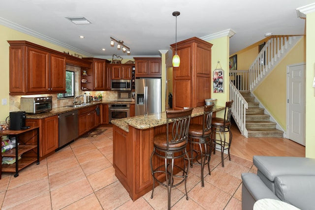 kitchen featuring light stone countertops, sink, stainless steel appliances, crown molding, and decorative light fixtures