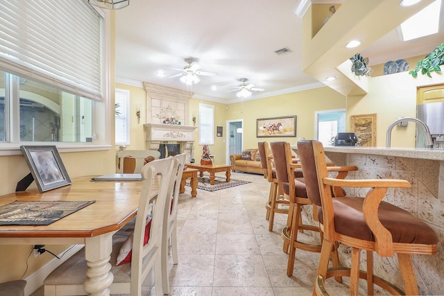 dining area with ceiling fan, a large fireplace, and ornamental molding