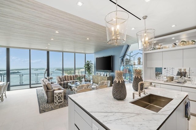 kitchen featuring sink, a wall of windows, white cabinets, light stone counters, and a water view