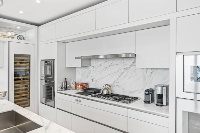 kitchen with wine cooler, light stone countertops, tasteful backsplash, white cabinetry, and stainless steel appliances