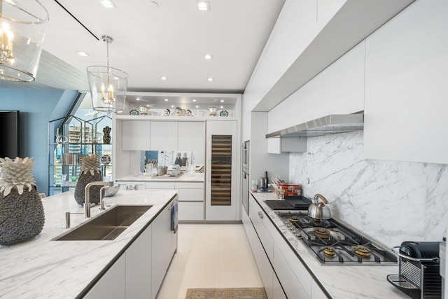 kitchen with light stone countertops, stainless steel gas cooktop, sink, decorative light fixtures, and white cabinetry