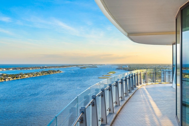 balcony at dusk featuring a water view