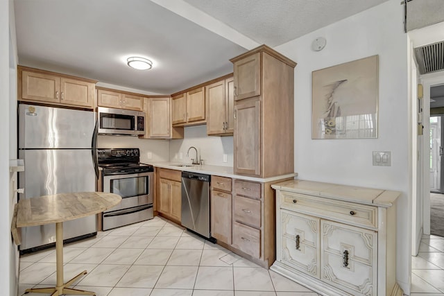 kitchen with sink, light brown cabinets, a textured ceiling, light tile patterned flooring, and appliances with stainless steel finishes