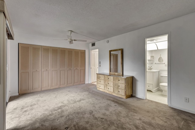 unfurnished bedroom with light carpet, ensuite bathroom, sink, ceiling fan, and a textured ceiling