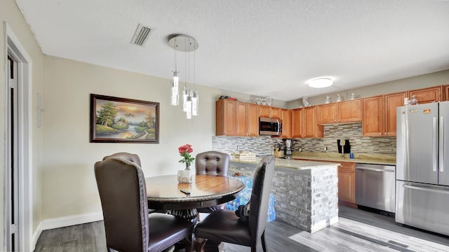 kitchen with backsplash, stainless steel appliances, hanging light fixtures, and light hardwood / wood-style flooring