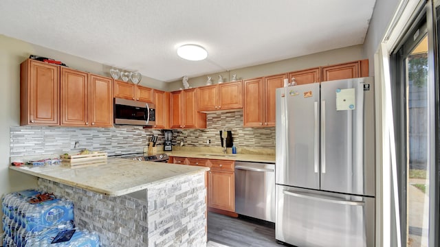 kitchen featuring hardwood / wood-style floors, sink, decorative backsplash, kitchen peninsula, and stainless steel appliances