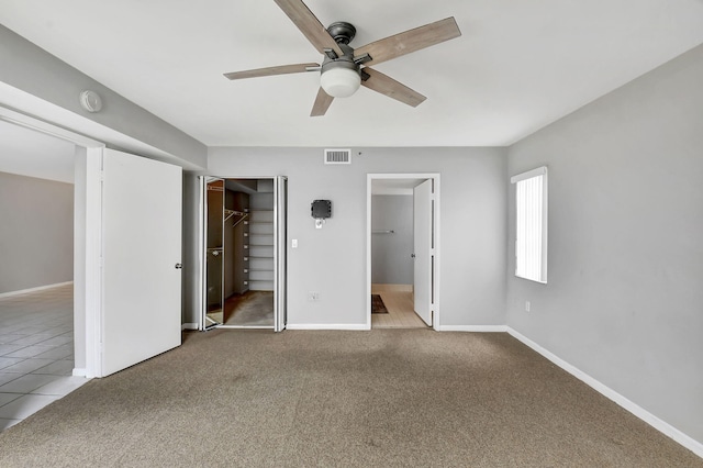 unfurnished bedroom with a walk in closet, carpet floors, a closet, and ceiling fan