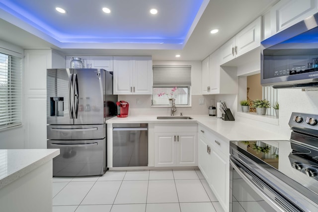 kitchen with appliances with stainless steel finishes, a tray ceiling, white cabinets, sink, and tasteful backsplash