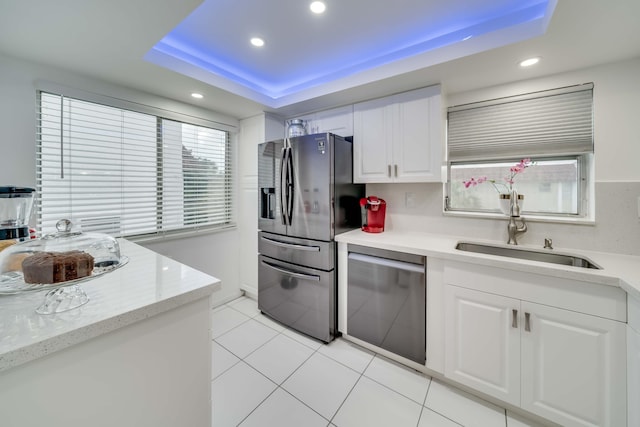 kitchen featuring a tray ceiling, white cabinets, sink, light tile floors, and appliances with stainless steel finishes