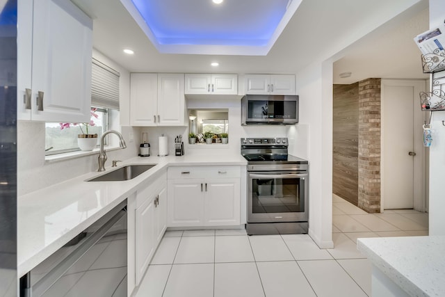 kitchen with appliances with stainless steel finishes, white cabinets, sink, light tile floors, and a raised ceiling