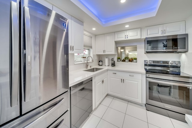 kitchen with a raised ceiling, white cabinetry, appliances with stainless steel finishes, sink, and light tile floors