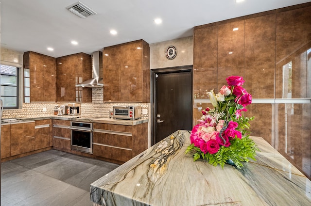 kitchen with wall chimney range hood, dark tile patterned floors, backsplash, oven, and black electric stovetop