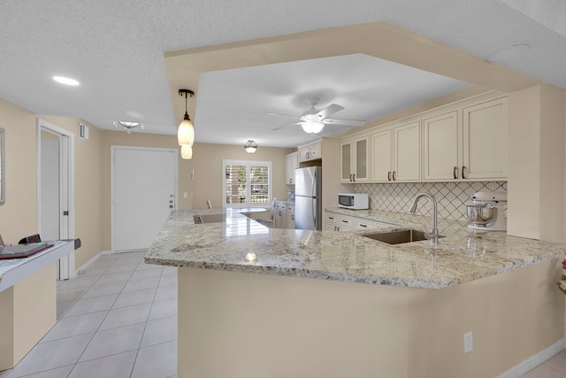 kitchen with kitchen peninsula, stainless steel fridge, light stone countertops, sink, and decorative light fixtures