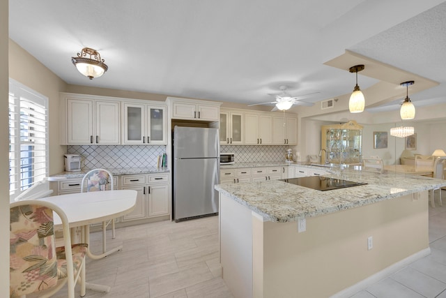 kitchen with kitchen peninsula, black electric stovetop, backsplash, decorative light fixtures, and stainless steel refrigerator