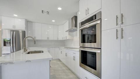 kitchen with tasteful backsplash, stainless steel appliances, wall chimney range hood, sink, and white cabinets