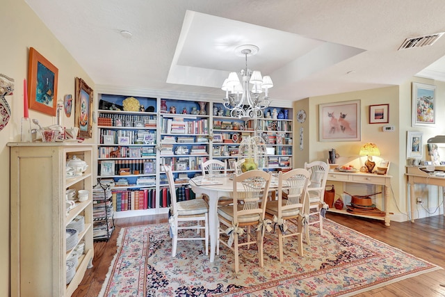 dining space featuring a tray ceiling, a textured ceiling, wood-type flooring, and a notable chandelier