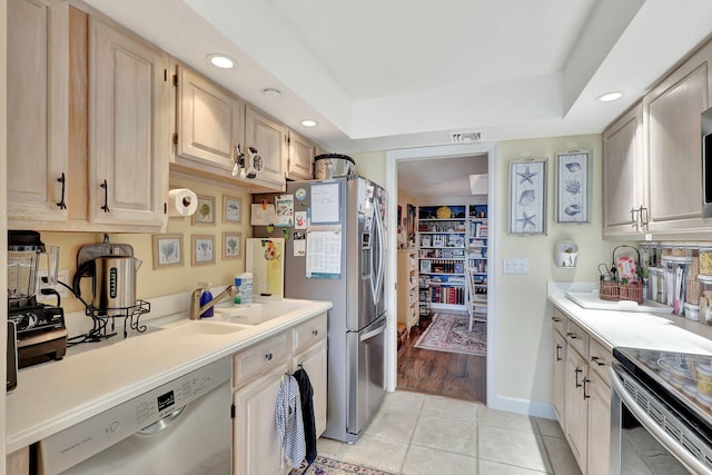 kitchen featuring a tray ceiling, stainless steel refrigerator with ice dispenser, sink, dishwasher, and light tile floors