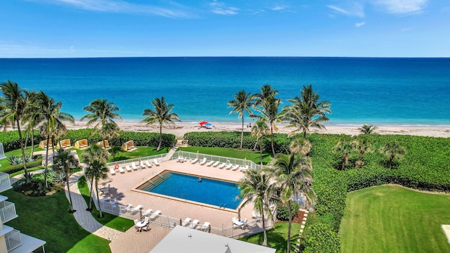 view of swimming pool featuring a view of the beach, a water view, and a lawn