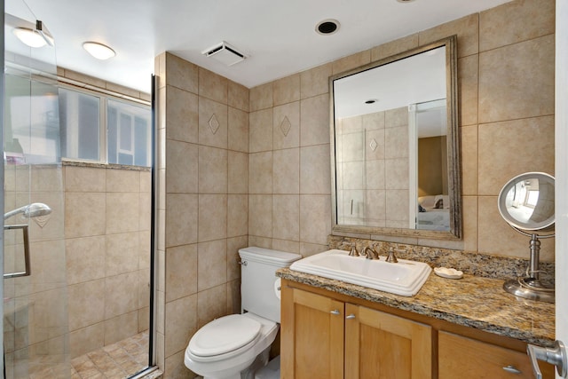 bathroom with a shower with door, vanity, toilet, and tile walls