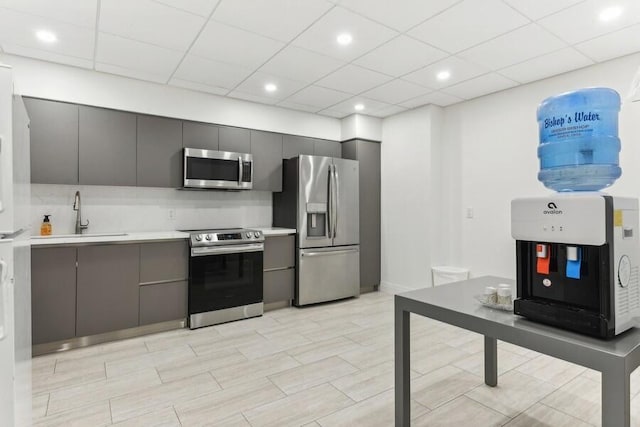 kitchen featuring appliances with stainless steel finishes, gray cabinets, a drop ceiling, and sink