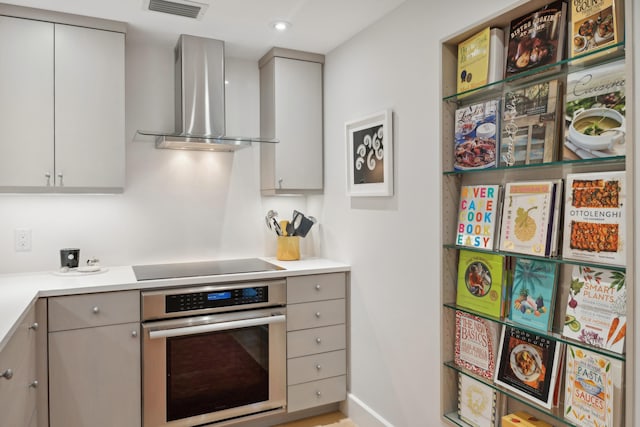 kitchen featuring black electric stovetop, stainless steel oven, gray cabinetry, and wall chimney range hood